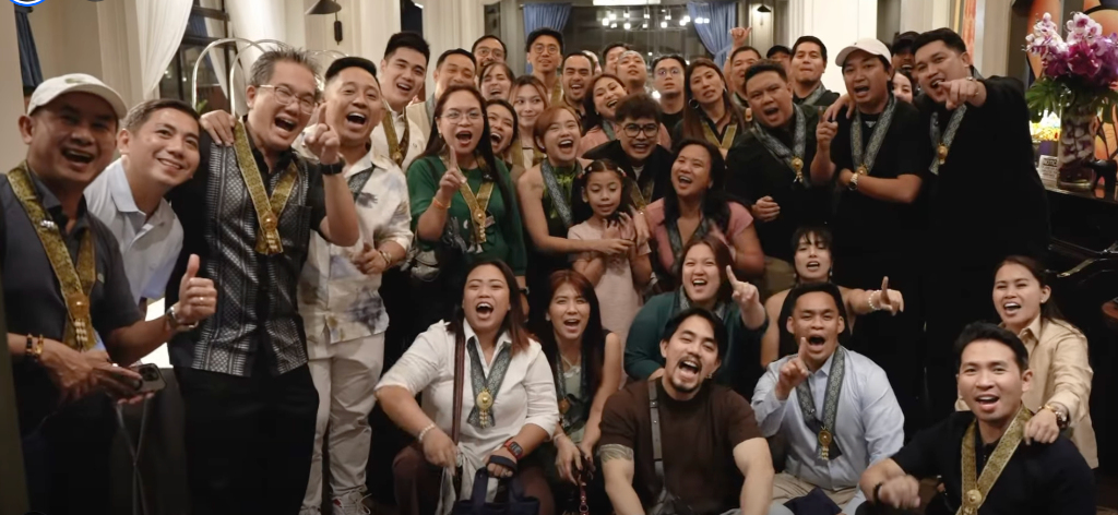 GCI members celebrating together at the Clarity to Legacy Davao event — laughing, pointing, and wearing gold medallions